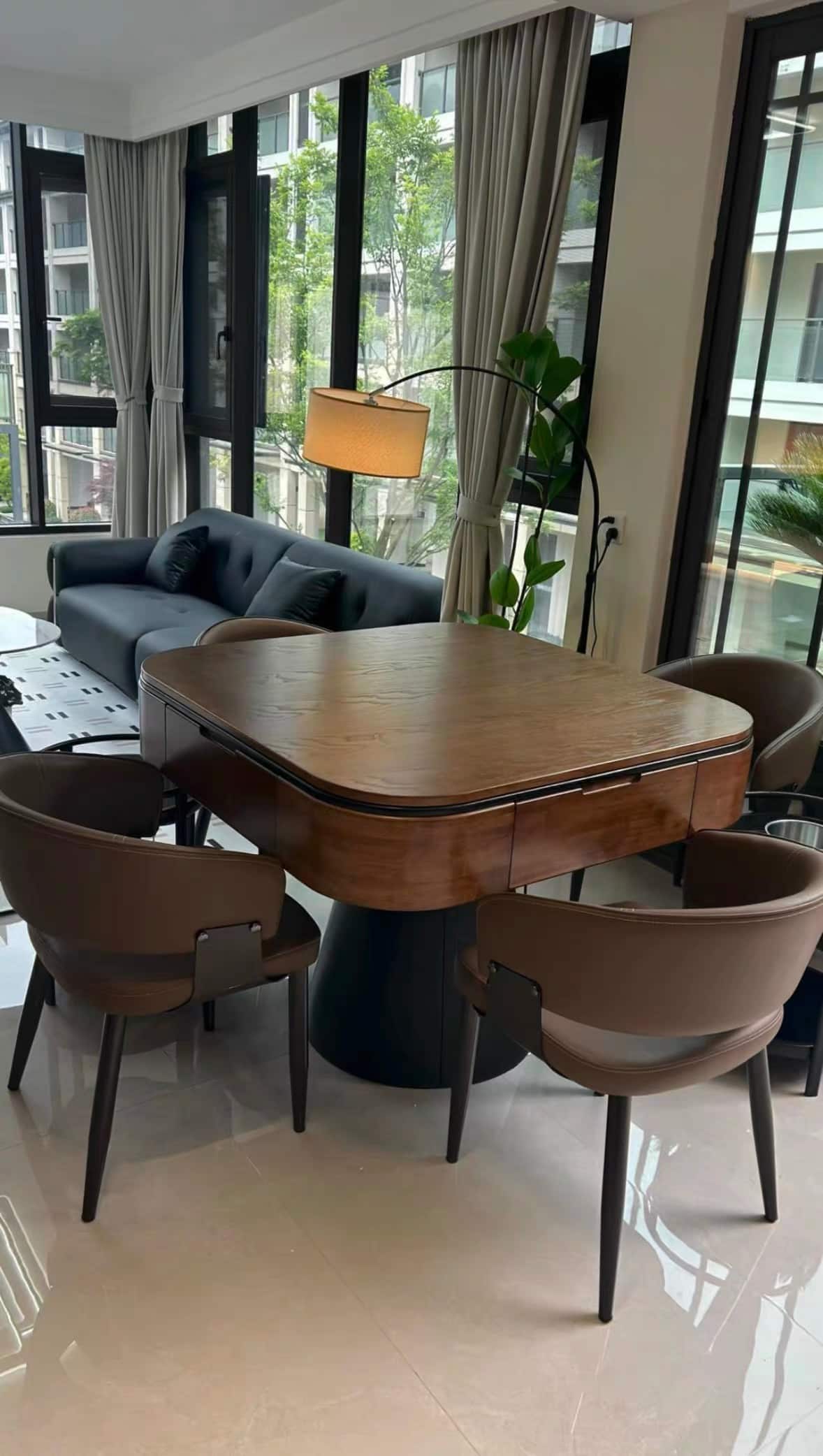 AURAJONG R5 automatic American Mahjong table with walnut finish and black pedestal base in a bright living room with large windows